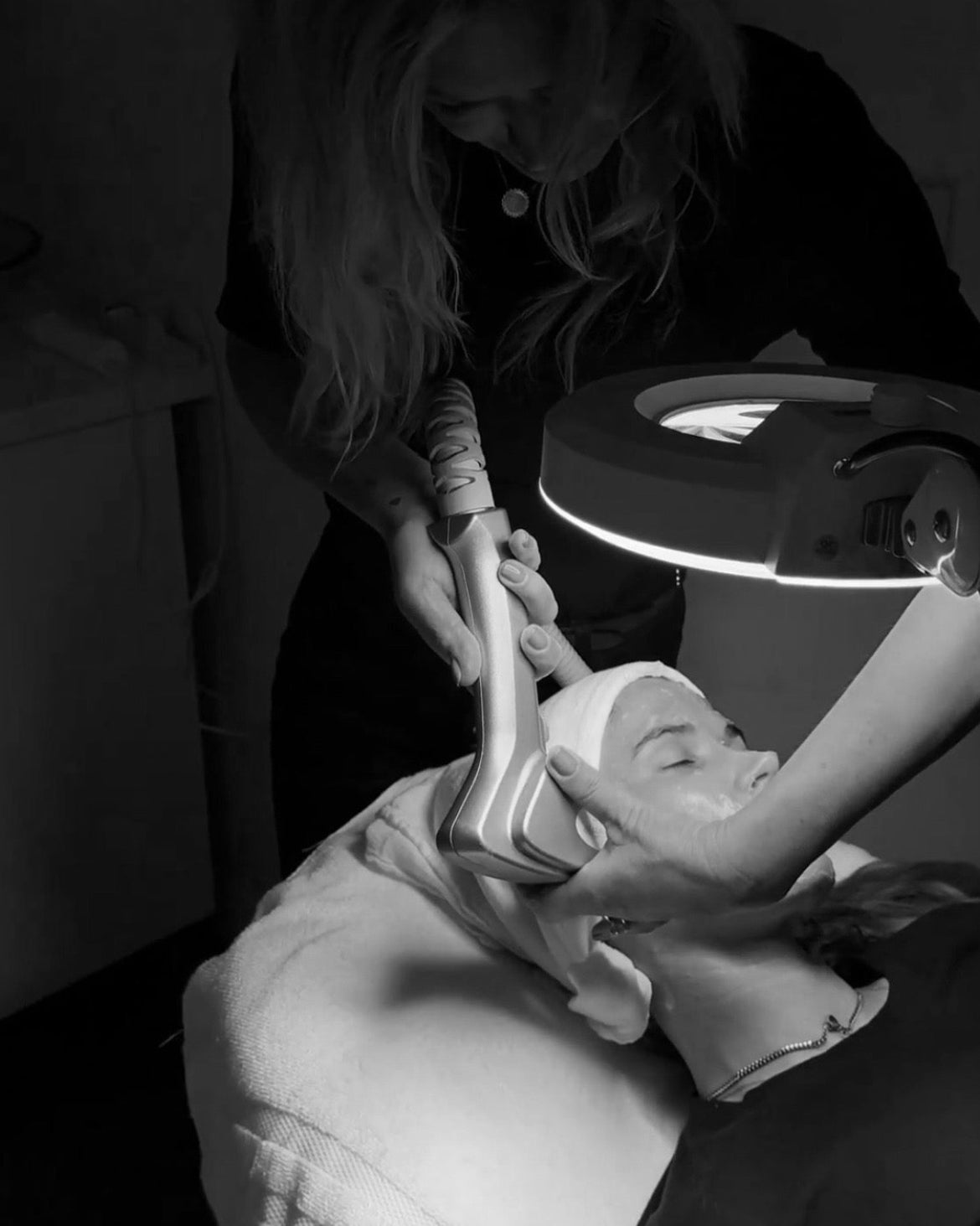 Person receiving a facial treatment with a lamp in a dimly lit room